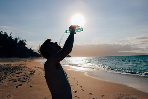 Person drinking water in the beach under the sun.