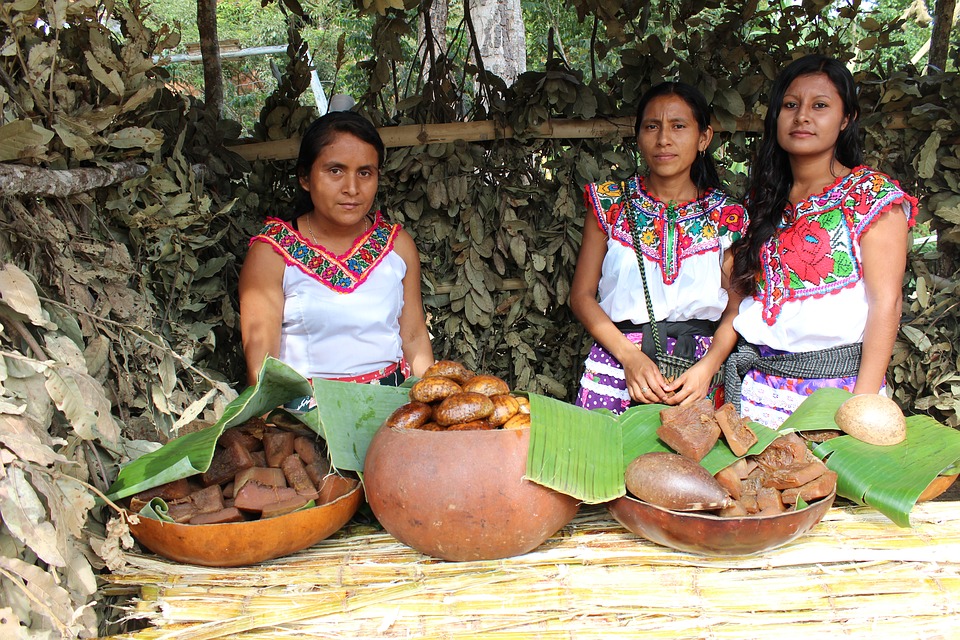 Mujeres indígenas en una choza pequeña junto a alimentos originarios