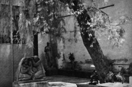 Fotografía blanco y negro del patio interior de la escuela La Esmeralda. Se observa un edificio y árbol viejo